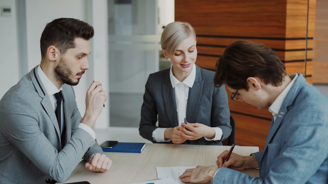 contact-hero Young businessman in suit signing contract with his colleague while corporate lawyer explaining details of partnership sitting in modern office indoors