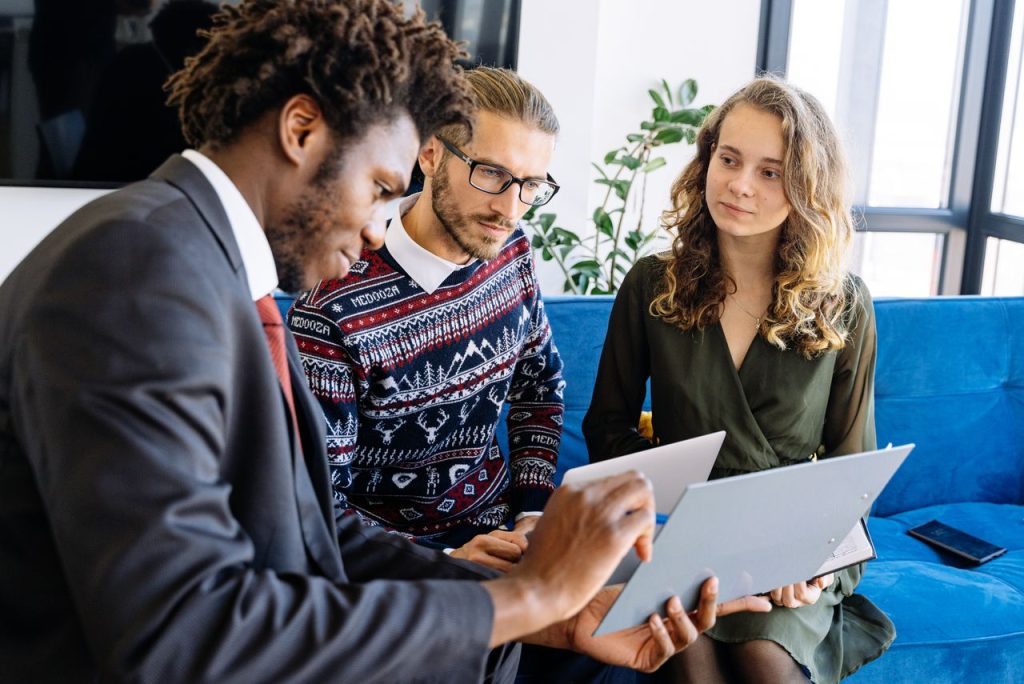 man-in-black-suit-jacket-holding-woman-in-blue-and-white-dress-5816297 A diverse group of young professionals engaged in a business meeting inside a modern office.
