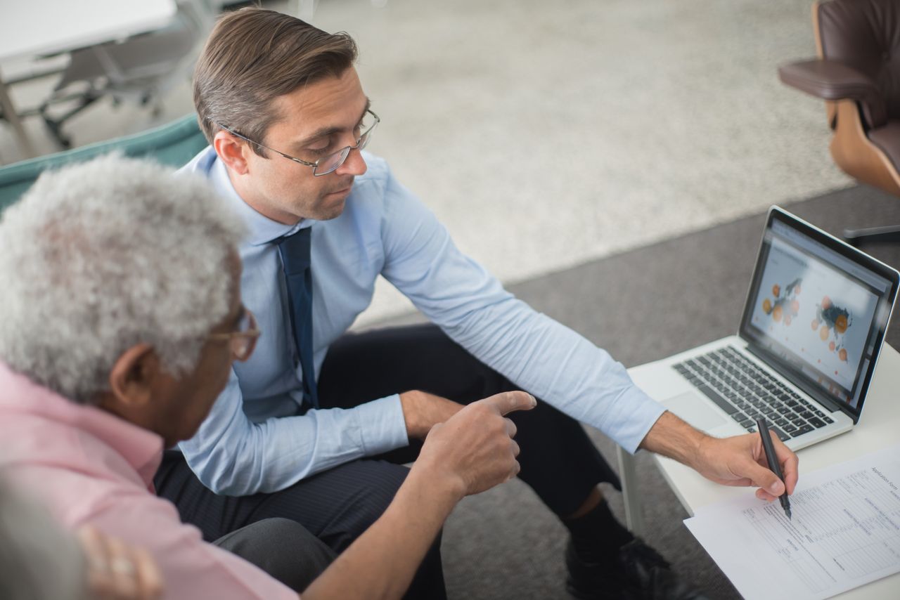 services-03 Two men in a business meeting reviewing financial documents and discussing data on a laptop.